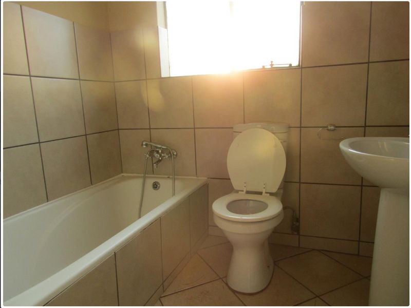A functional bathroom featuring a bathtub, pedestal basin, and toilet with neutral wall and floor tiling.