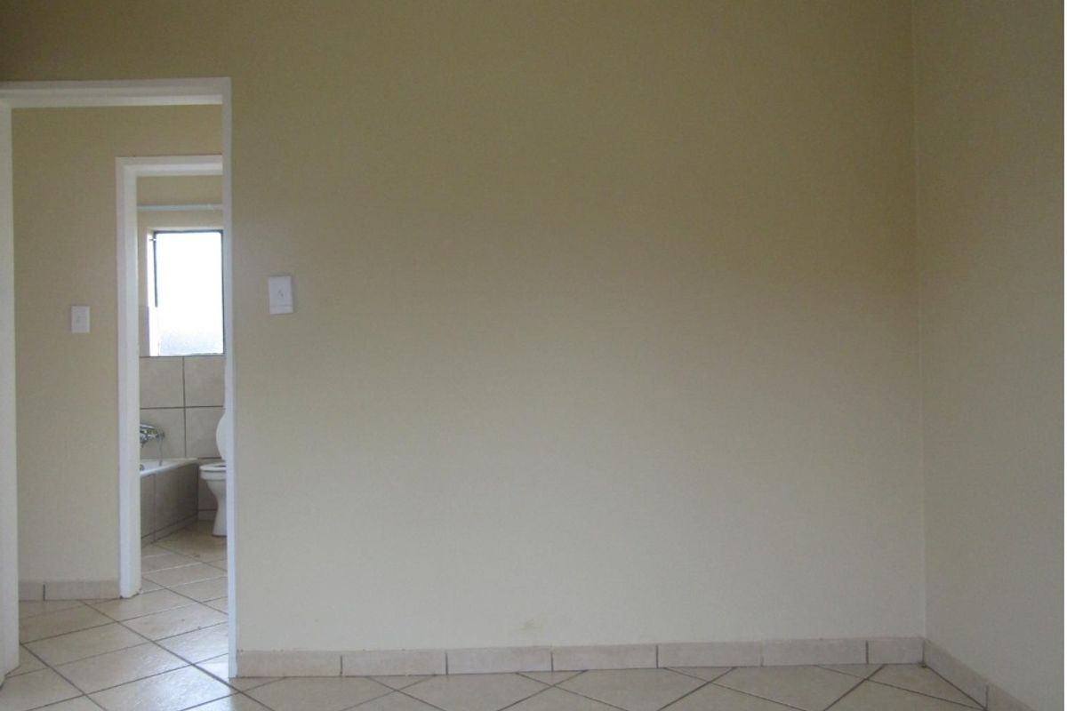 An empty bedroom featuring neutral wall paint and tiled flooring, with a direct view into an adjacent bathroom.
