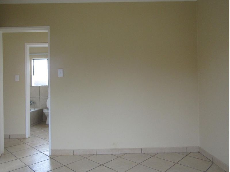 An empty bedroom featuring neutral wall paint and tiled flooring, with a direct view into an adjacent bathroom.