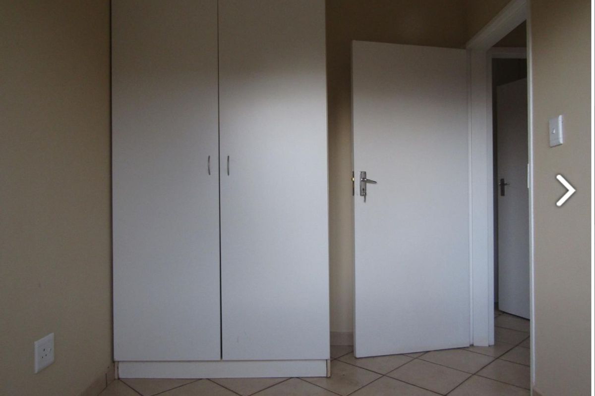 A simple bedroom featuring neutral walls, tiled flooring, and a built-in wardrobe, offering a clean and functional space.