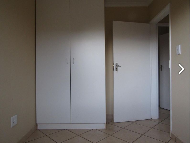 A simple bedroom featuring neutral walls, tiled flooring, and a built-in wardrobe, offering a clean and functional space.