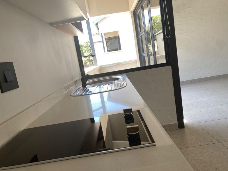 Modern kitchen featuring a sleek quartz countertop, built-in electric hob, stainless steel sink, and contemporary black fixtures, opening onto an adjacent living area.