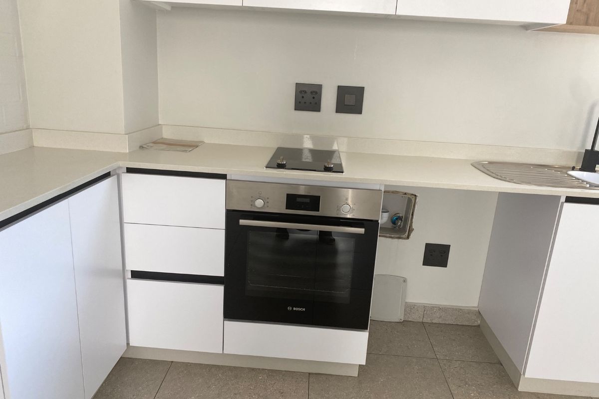 Modern kitchen featuring white cabinetry, stone countertops, built-in oven, and electric hob, with an open space ready for an integrated appliance.