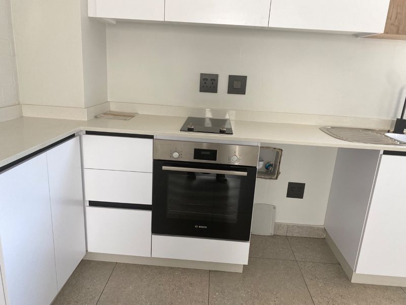Modern kitchen featuring white cabinetry, stone countertops, built-in oven, and electric hob, with an open space ready for an integrated appliance.