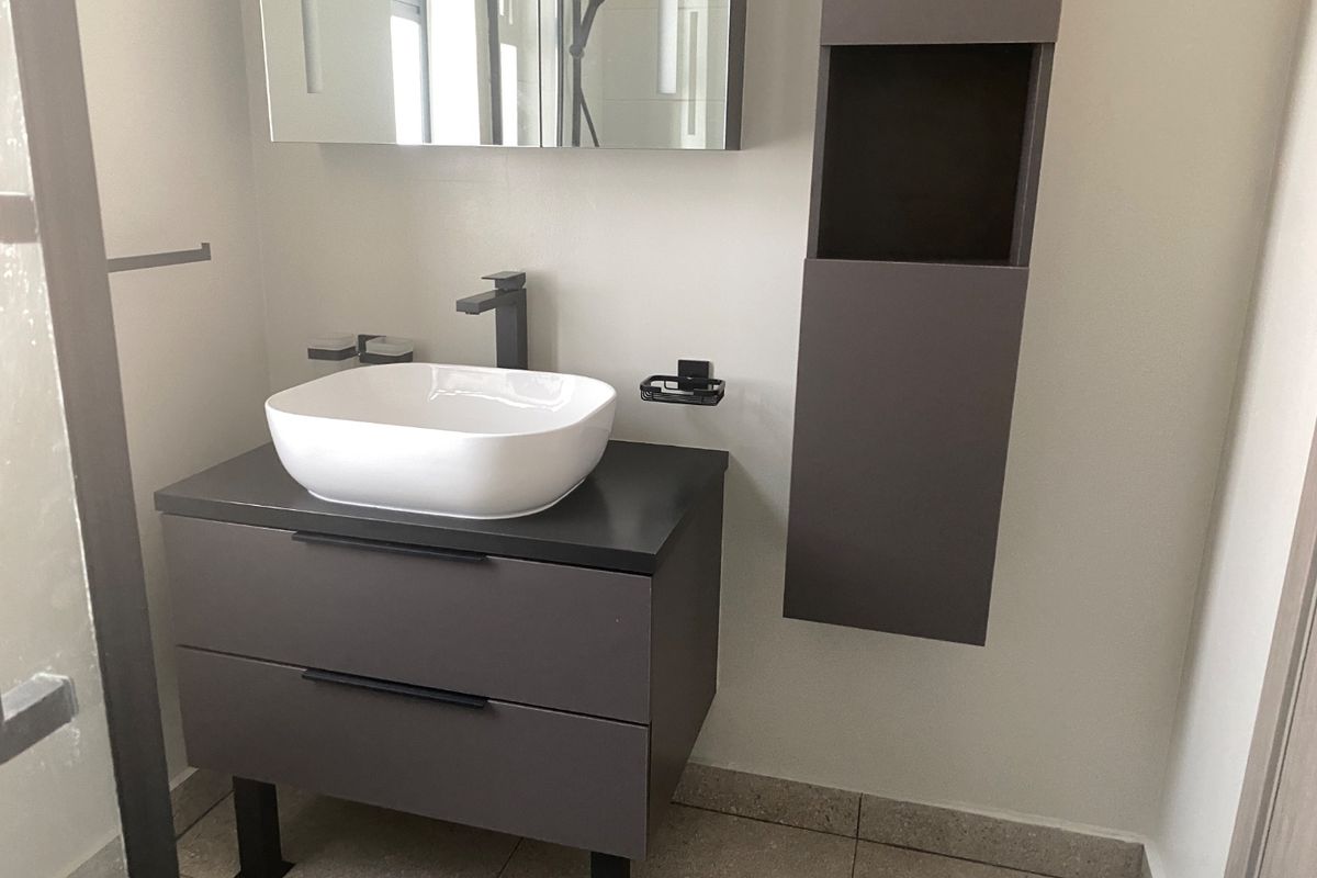Modern bathroom featuring a contemporary vessel sink, dark grey vanity cabinet, wall-mounted storage, and a sleek mirror cabinet with integrated lighting.