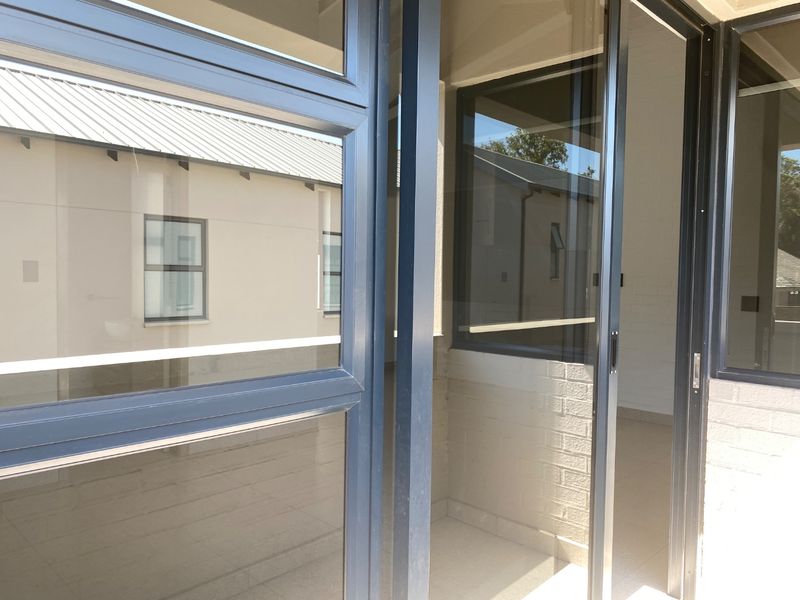 A covered patio area featuring modern dark-framed sliding glass doors and neutral tiled flooring, providing a seamless transition to the interior space.