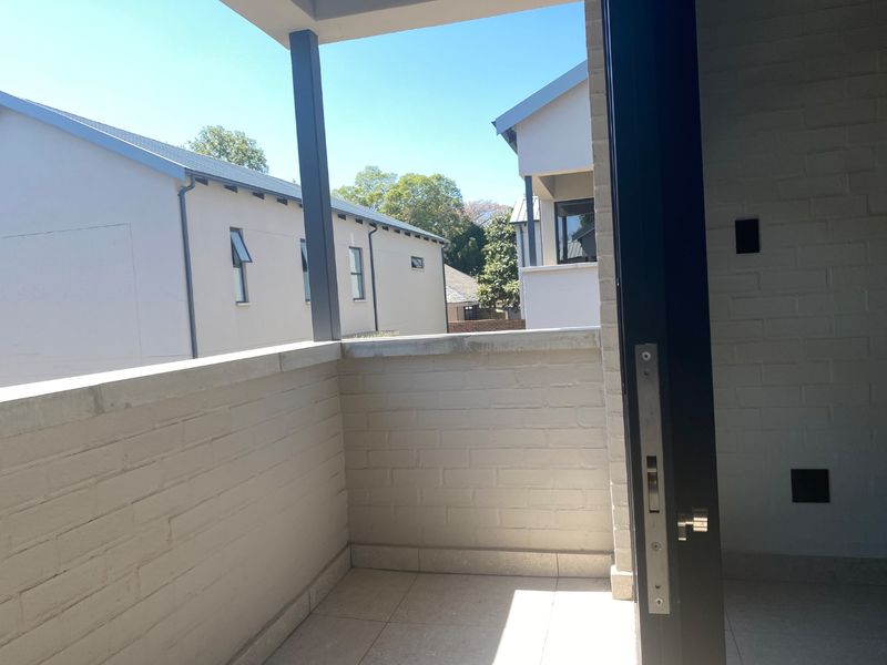 A clean, modern balcony featuring tiled flooring, painted brick walls, and a metal support pillar, offering an open outdoor space.