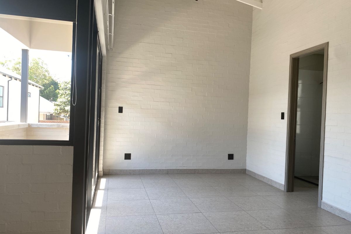 A bright, empty living area featuring vaulted ceilings, exposed white brick walls, tiled flooring, and large sliding glass doors leading to an outdoor space.
