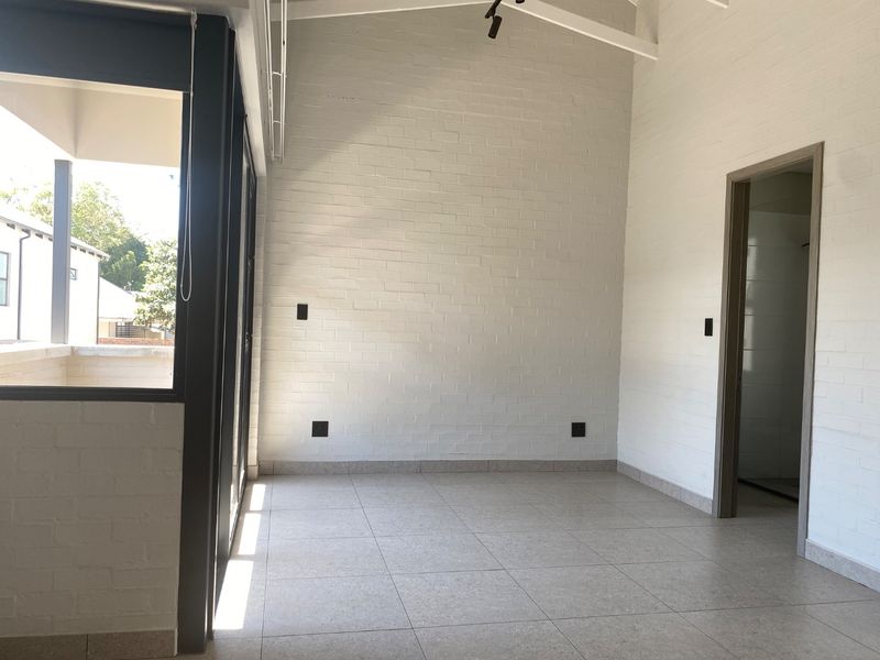 A bright, empty living area featuring vaulted ceilings, exposed white brick walls, tiled flooring, and large sliding glass doors leading to an outdoor space.