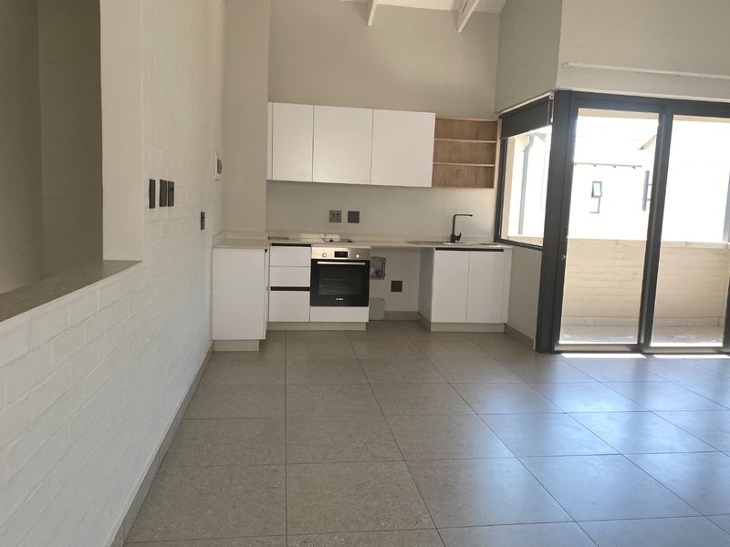 Modern open-plan kitchen featuring white cabinetry, built-in oven, and tiled flooring, seamlessly connecting to a bright balcony through large sliding glass doors.