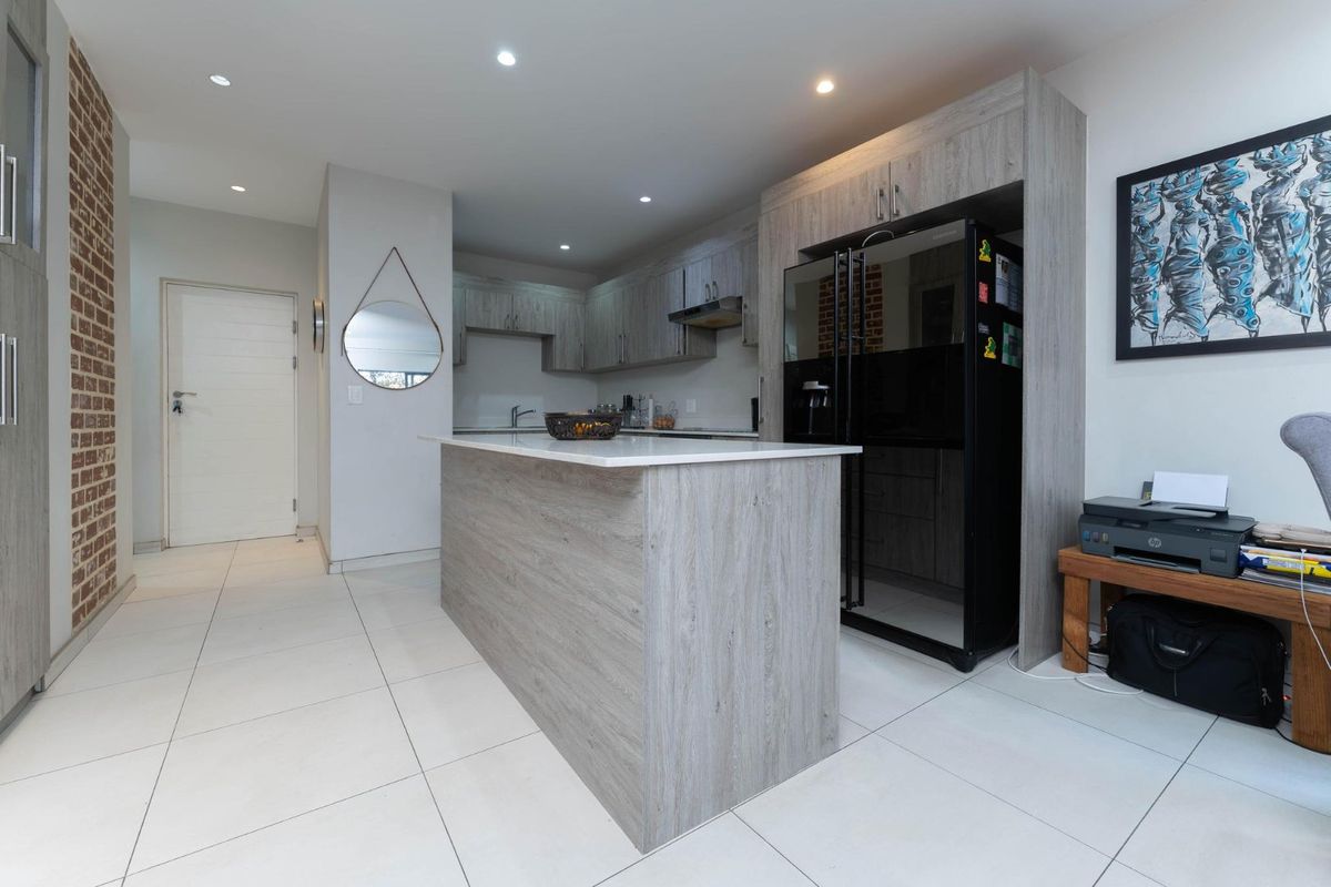 Modern kitchen featuring a central island, light wood-grain cabinetry, recessed lighting, and an exposed brick accent wall, creating a contemporary and functional space.