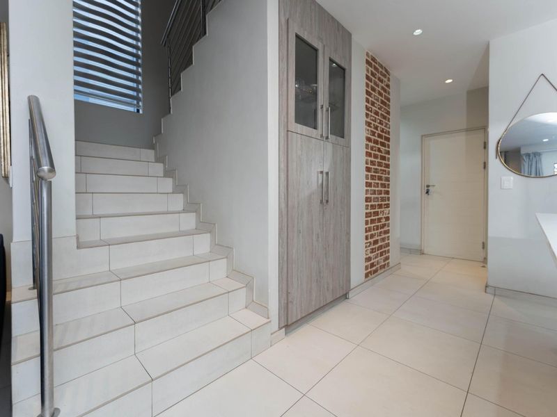 Modern hallway featuring a tiled staircase with stainless steel balustrade, built-in storage cabinetry, and an exposed brick feature wall.