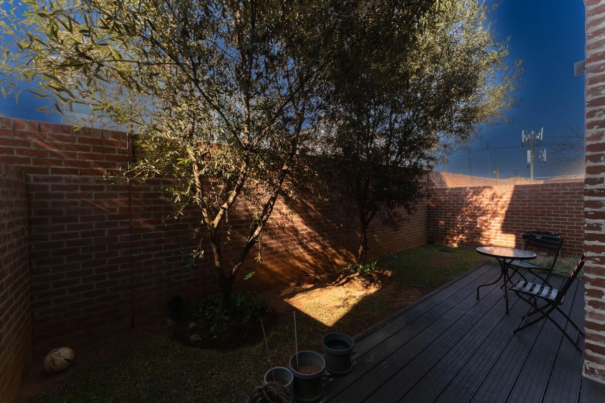A private rear garden featuring a timber deck, established trees, and secure brick boundary walls, providing a quiet outdoor space.