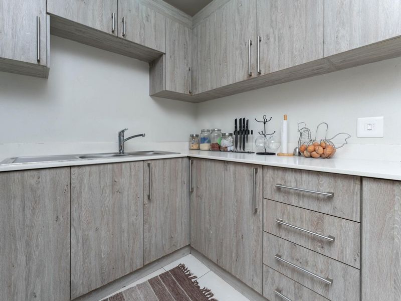 A modern kitchen featuring light wood-grain laminate cabinetry, stone countertops, and a stainless steel sink with a contemporary mixer tap.