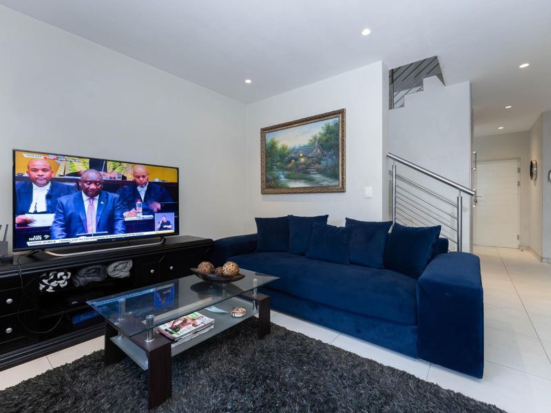 A modern living room featuring tiled flooring, recessed downlights, and a staircase with a stainless steel railing.