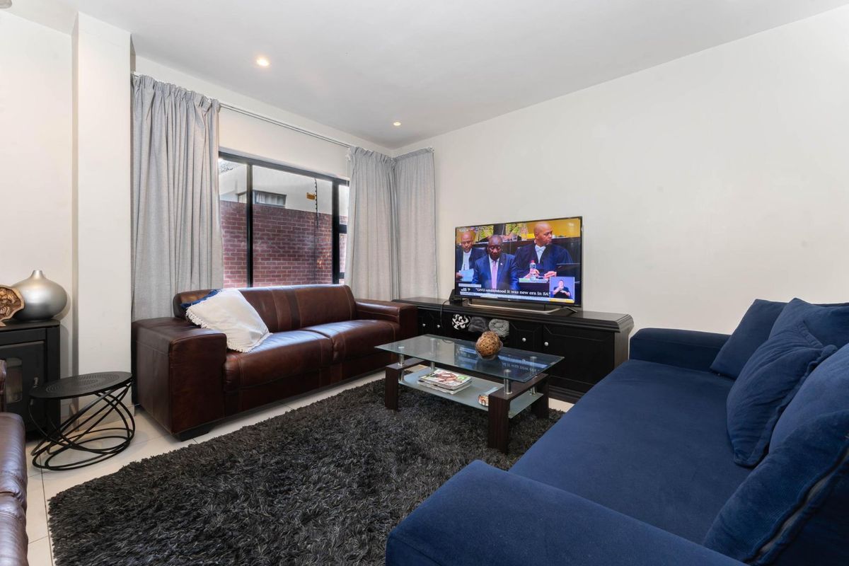 A comfortable living room featuring tiled flooring, recessed downlighting, and a large window with views of the exterior brick wall.