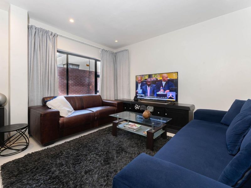 A comfortable living room featuring tiled flooring, recessed downlighting, and a large window with views of the exterior brick wall.