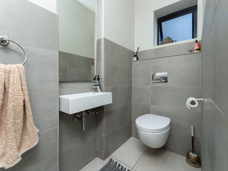 Modern guest bathroom featuring grey wall and floor tiles, a wall-mounted basin, and a concealed cistern toilet.