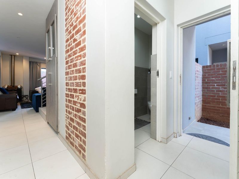 A bright hallway featuring modern tiled flooring and an exposed brick accent wall, providing access to adjacent living areas and an outdoor courtyard.