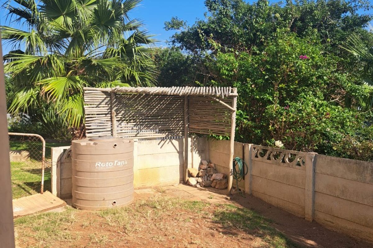 A rear outdoor area featuring a concrete block boundary wall, a water storage tank, and a timber pergola structure set within a garden space.