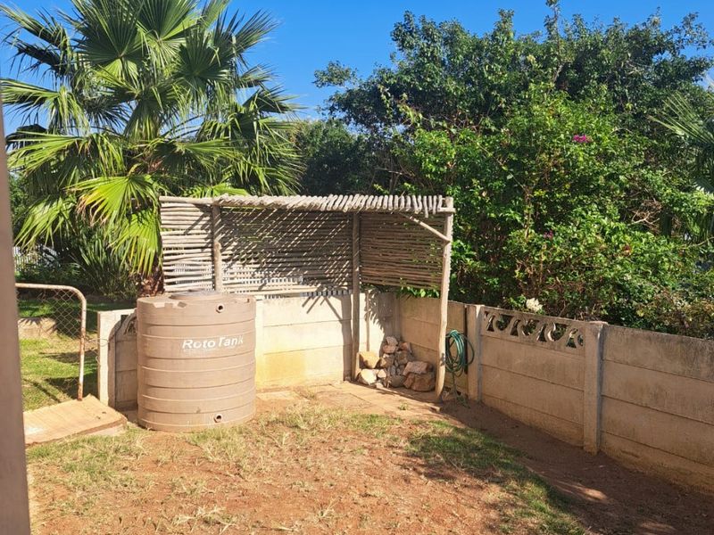 A rear outdoor area featuring a concrete block boundary wall, a water storage tank, and a timber pergola structure set within a garden space.