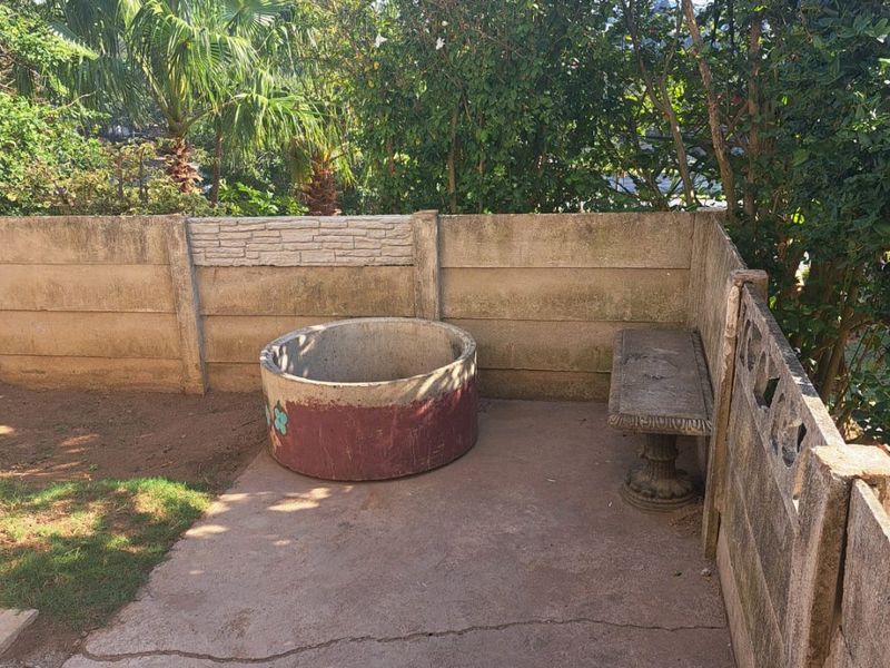 A private garden area featuring a concrete patio, boundary wall, and built-in concrete bench, offering potential for landscaping and outdoor improvement.