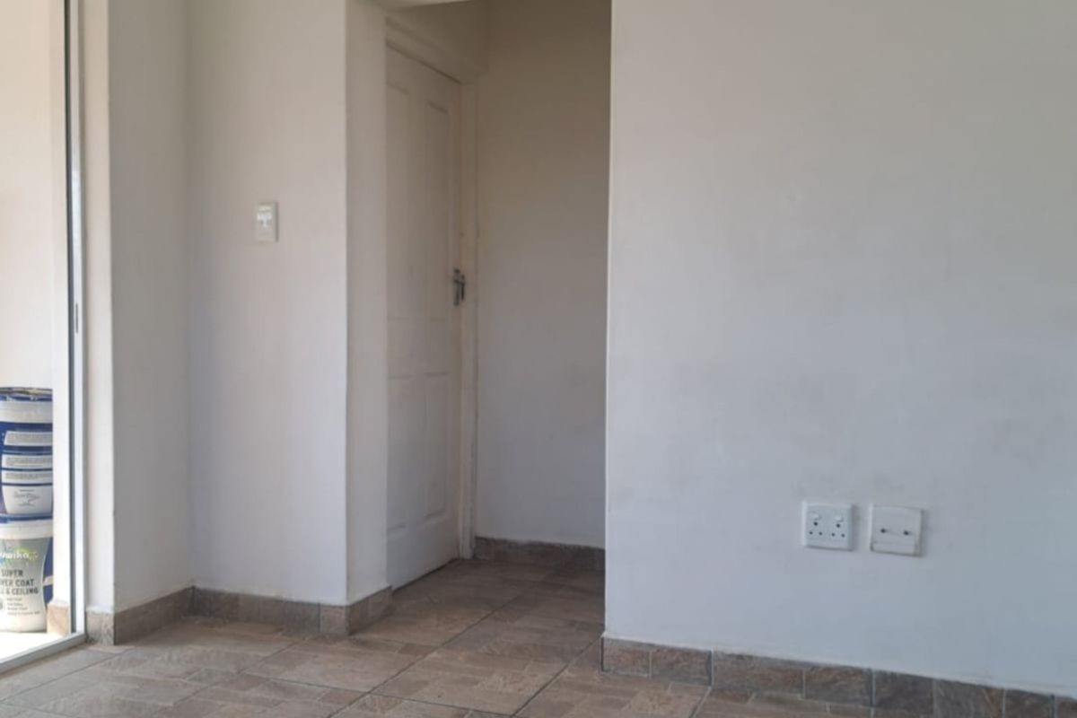 An empty living area featuring tiled flooring, neutral walls, and a sliding glass door providing access to an outdoor space.