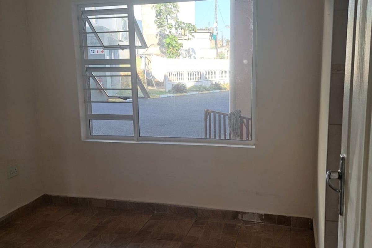 An empty bedroom featuring tiled flooring, a large aluminium louvered window, and neutral wall finishes, offering a blank canvas for personalization.