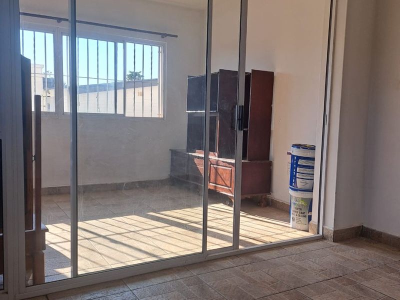 An enclosed balcony or sunroom featuring tiled flooring, large sliding glass doors, and security bars on the windows, offering a bright, versatile space.