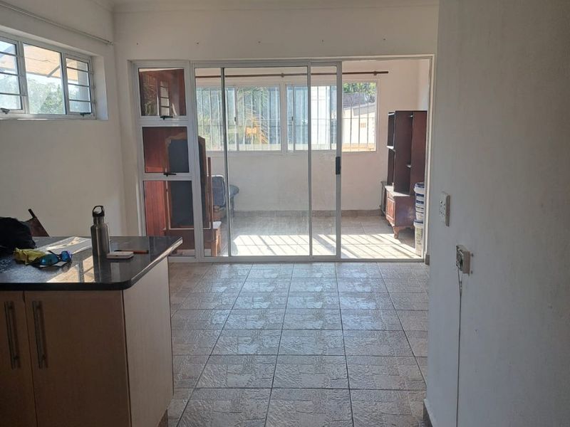 Open plan living area featuring tiled flooring, kitchen cabinetry with granite countertops, and sliding glass doors leading to an enclosed balcony.