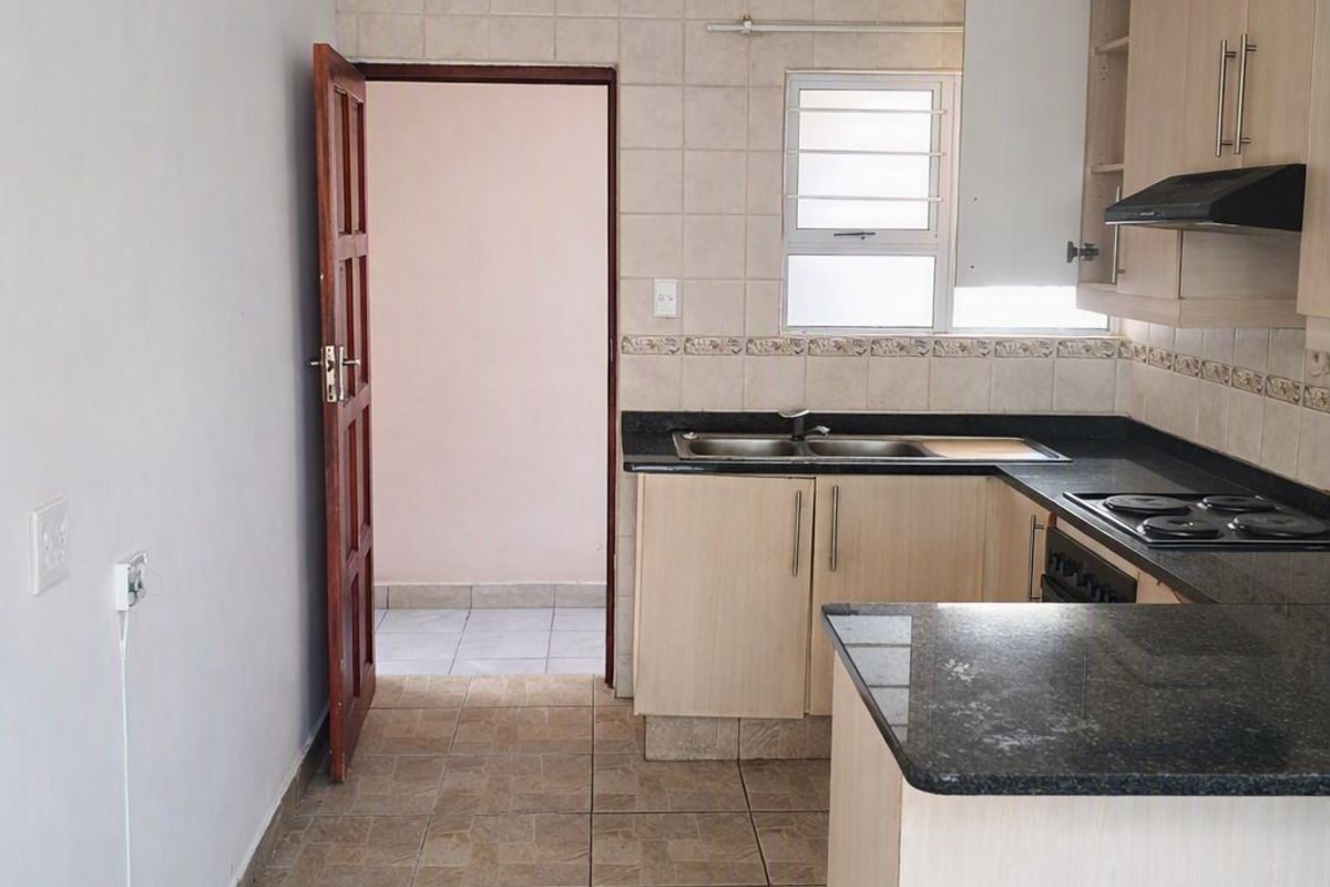 A functional kitchen featuring light wood cabinetry, dark granite countertops, a built-in hob, and tiled flooring, offering a clean and practical workspace.