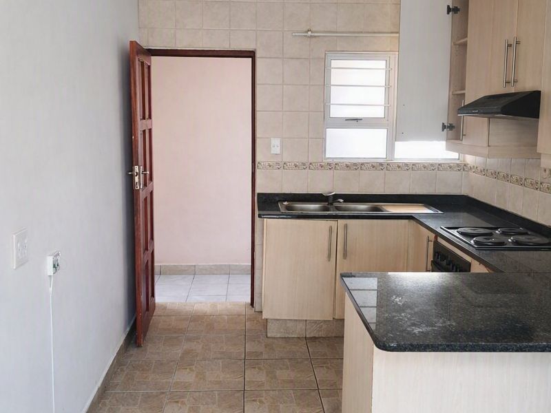 A functional kitchen featuring light wood cabinetry, dark granite countertops, a built-in hob, and tiled flooring, offering a clean and practical workspace.