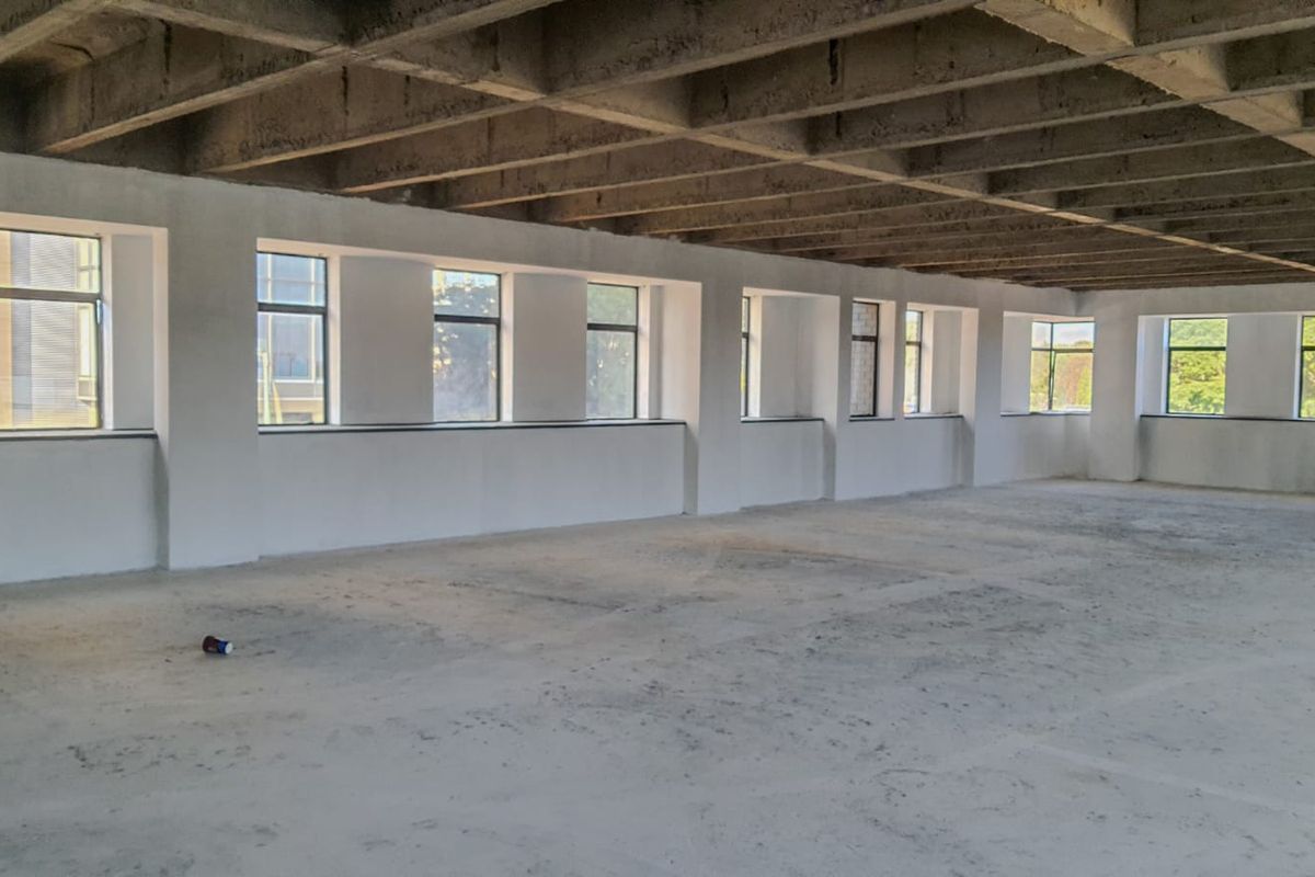 A large, open-plan commercial space featuring exposed concrete ceiling beams, concrete flooring, and a series of large windows providing ample natural light.