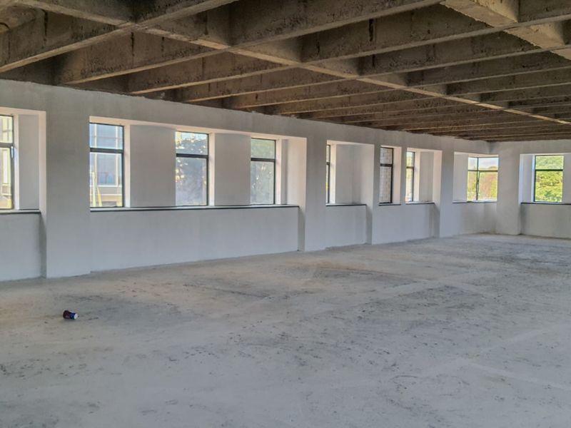 A large, open-plan commercial space featuring exposed concrete ceiling beams, concrete flooring, and a series of large windows providing ample natural light.