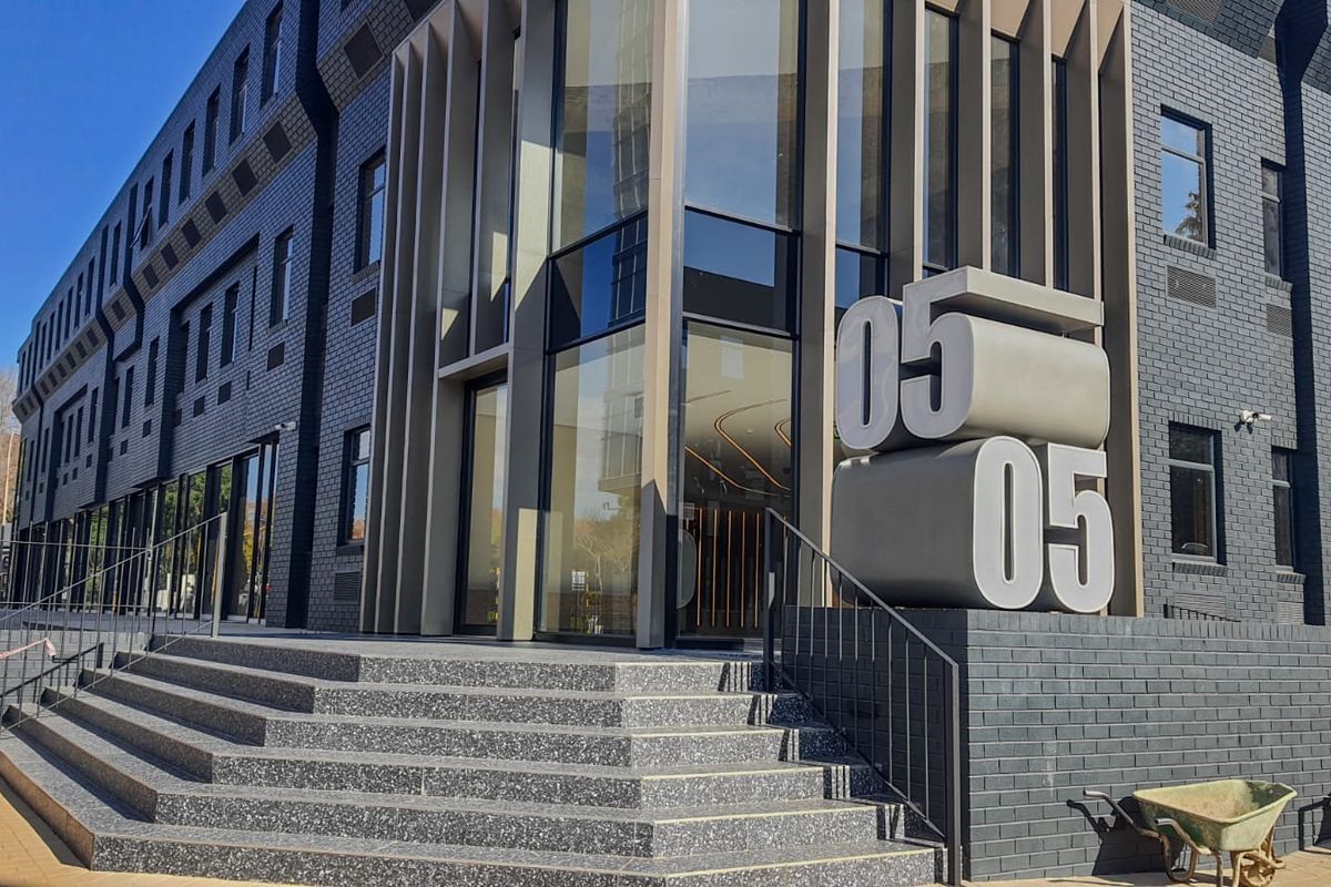 Modern commercial building exterior featuring a dark brick facade, prominent glass entrance, and architectural signage with stone-finished steps.