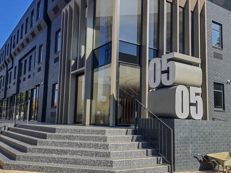 Modern commercial building exterior featuring a dark brick facade, prominent glass entrance, and architectural signage with stone-finished steps.
