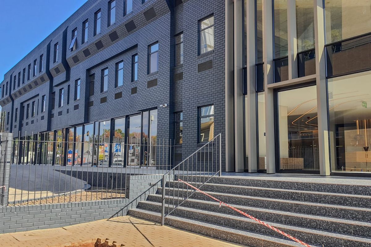 Modern commercial building exterior featuring a dark brick facade, expansive glass frontage, and a prominent entrance with terrazzo steps and metal railings.