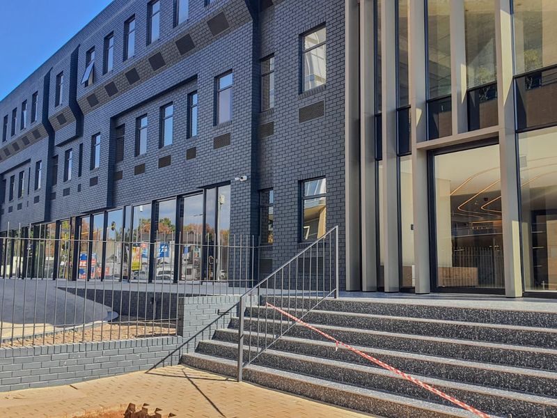 Modern commercial building exterior featuring a dark brick facade, expansive glass frontage, and a prominent entrance with terrazzo steps and metal railings.