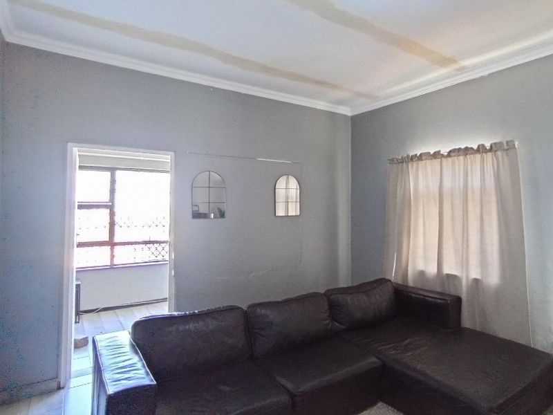 Living room featuring coved ceilings and access to an adjoining balcony, showing visible signs of ceiling water damage and wall plaster cracking.
