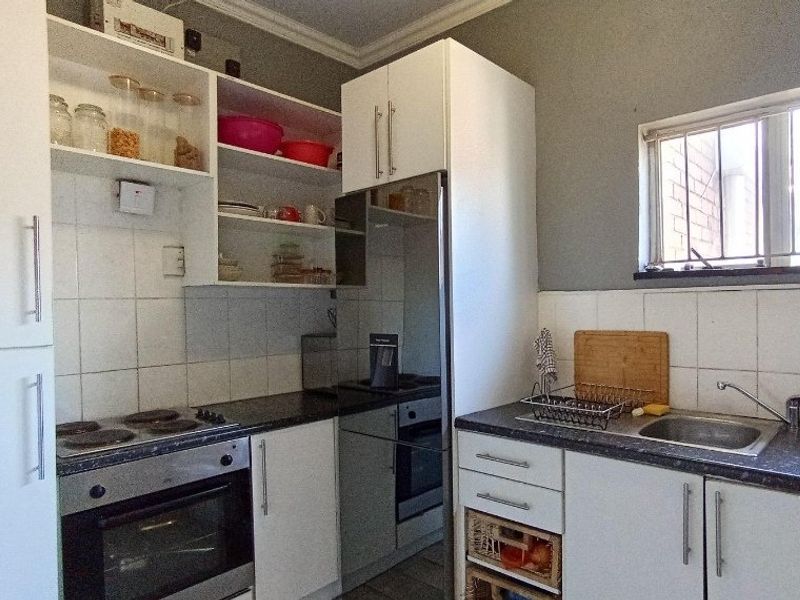 Compact kitchen featuring built-in oven, electric hob, stainless steel sink, laminate countertops, and ample white cabinetry with open shelving.
