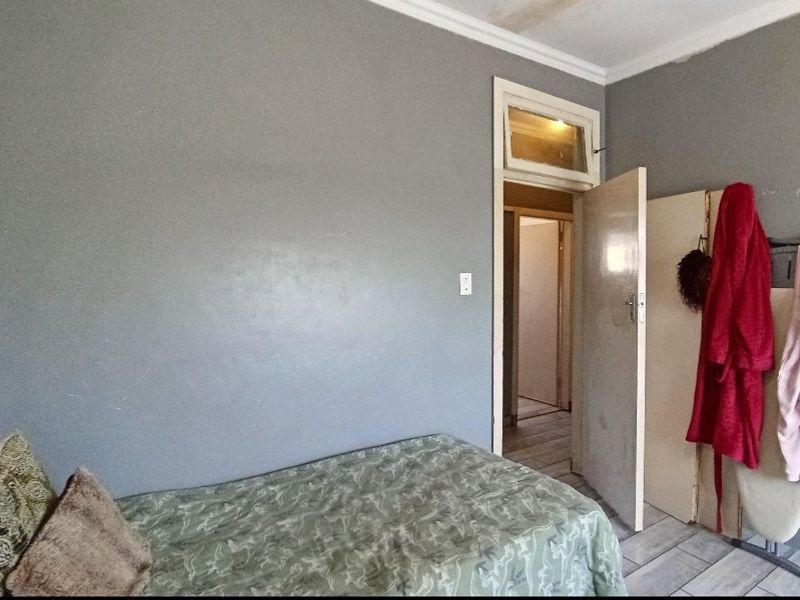 A bedroom featuring tiled flooring, a transom window above the door, and coving detail, requiring cosmetic updates to the wall finishes.