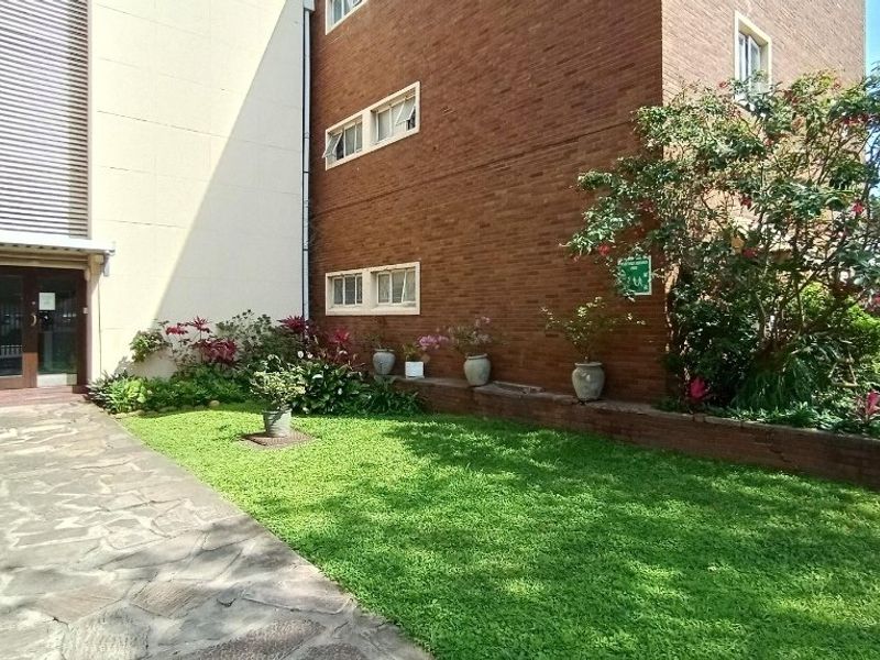 A well-maintained rear exterior view of the apartment building featuring a brick facade, stone paved walkway, and a landscaped garden area.