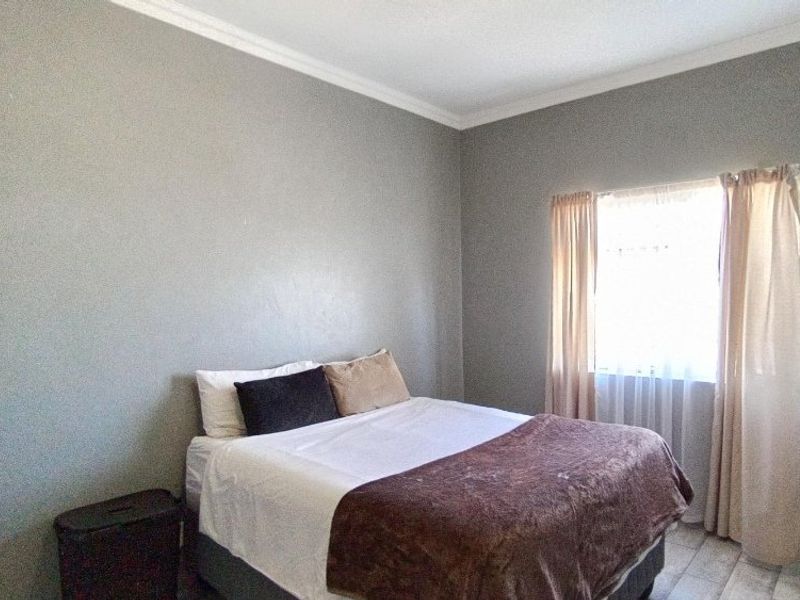 A simple bedroom featuring neutral grey walls, crown molding, and tiled flooring, providing a clean and functional space.