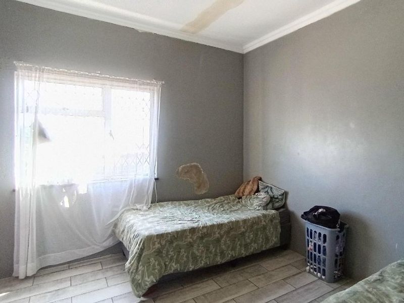 A bedroom featuring tiled flooring and a window with security bars, currently showing signs of wall and ceiling damage requiring maintenance.