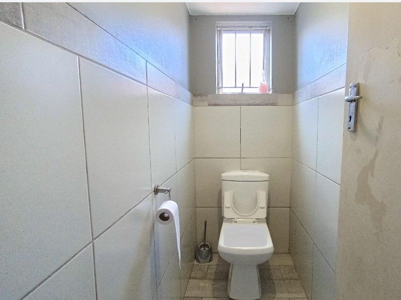 A compact, tiled bathroom featuring a standard toilet and a small window with security bars.