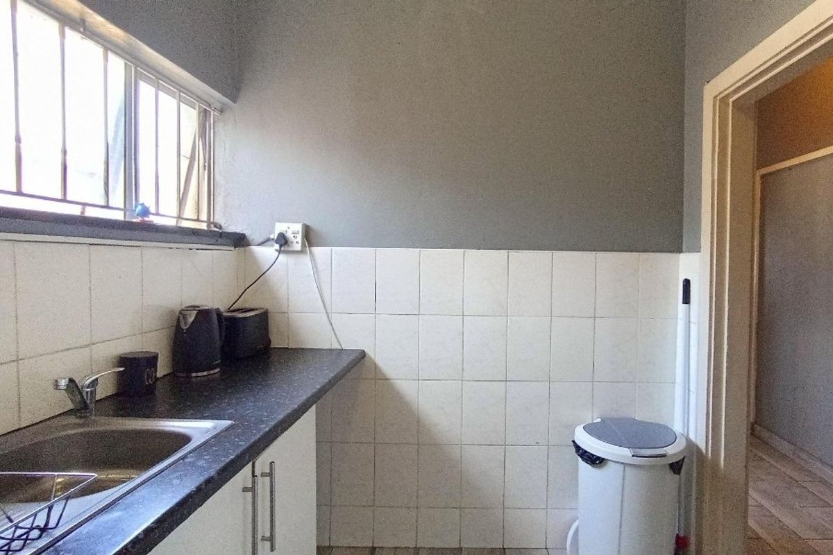 A functional kitchen area featuring a stainless steel sink, laminate countertops, and tiled splashbacks, with security bars installed on the window.