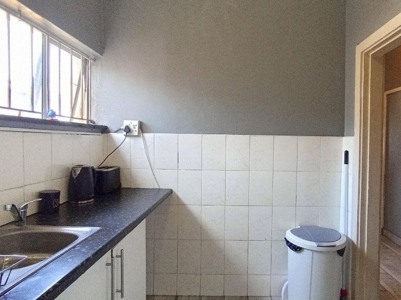 A functional kitchen area featuring a stainless steel sink, laminate countertops, and tiled splashbacks, with security bars installed on the window.