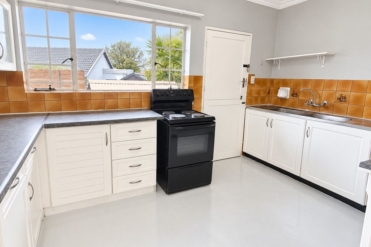 A functional kitchen featuring white cabinetry, laminate countertops, a tiled splashback, and a freestanding electric stove with natural light from large windows.