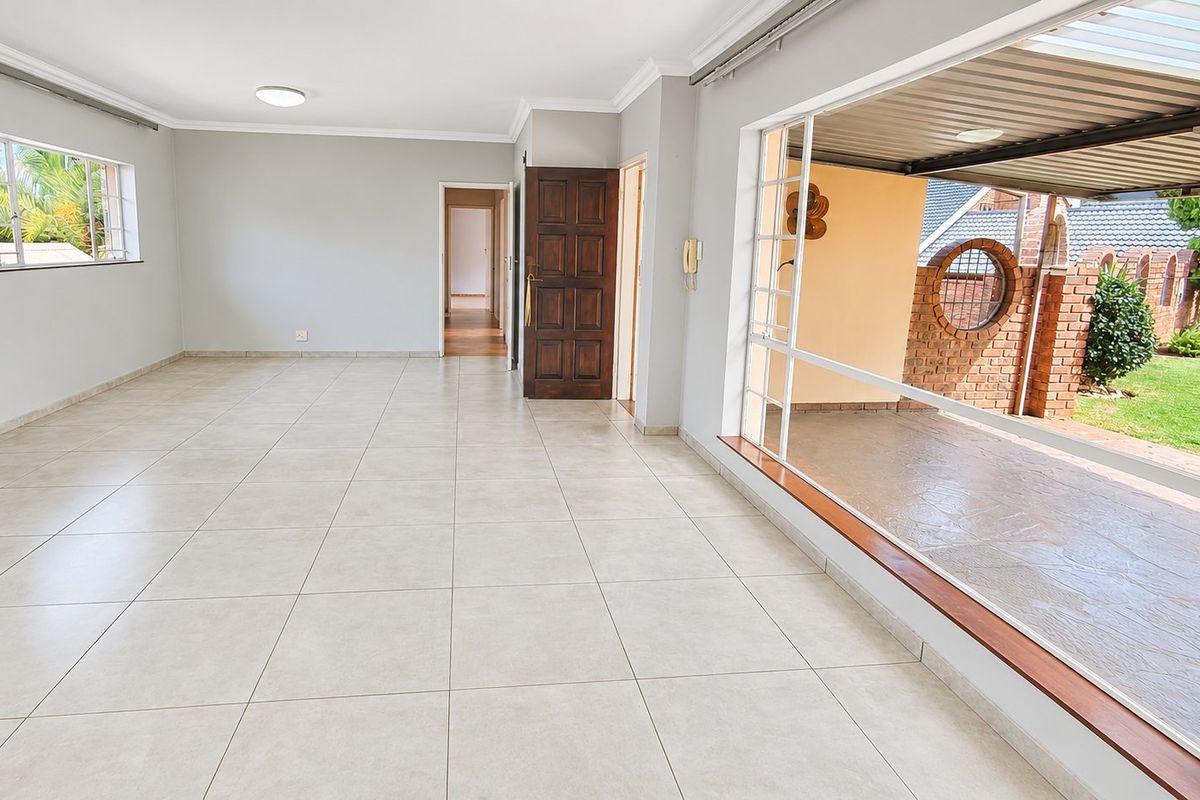Spacious, light-filled living area featuring neutral tiled flooring, large sliding doors opening to a patio, and clean, well-maintained finishes throughout.
