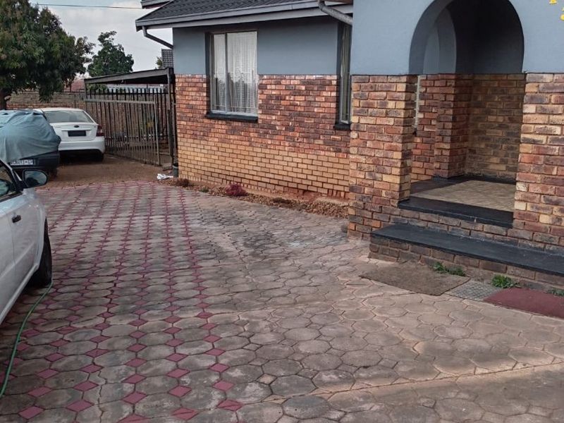 Front exterior view of a house featuring a brick and painted facade, an arched entrance, and a paved driveway.